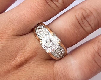 Op de afbeelding: Een gouden ring met een grote, heldere steen omringd door kleinere, heldere stenen.