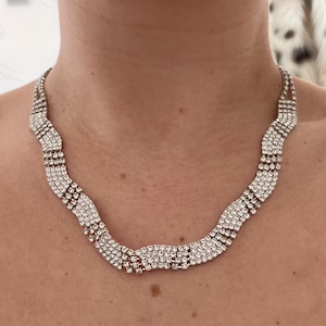 May include: A silver necklace with a wavy design made of small, clear rhinestones.