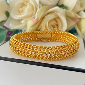 Puede incluir: Un brazalete de cadena de oro con una doble fila de eslabones entrelazados. El brazalete tiene un cierre de broche.