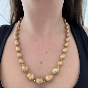 Könnte beinhalten: Eine goldene Halskette mit ovalen Perlen. Die Perlen haben eine strukturierte, gebürstete Oberfläche.