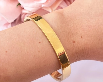 Puede incluir: Un brazalete de oro con un acabado liso y pulido. El brazalete está abierto y tiene un diseño simple y minimalista.