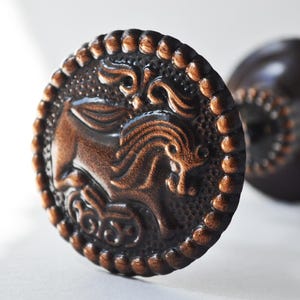 May include: A pair of decorative curtain rod finials with a bronze finish. One finial features a detailed design of a winged horse with intricate scrollwork.