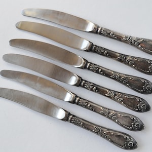 May include: Set of six silver-plated dinner knives with ornate handles. The knives have a classic design and are in good condition.