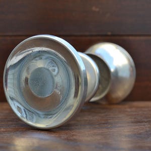 Può includere: Un oggetto decorativo color argento con una base arrotondata e una parte superiore bulbosa. L'oggetto ha una superficie riflettente ed è posizionato su una superficie di legno. Il design suggerisce un'estetica vintage o antica.