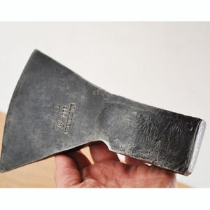 Peut inclure: Une tête de hache en métal gris foncé avec un tranchant large et incurvé et une tête rectangulaire. Le côté de la tête de hache présente des marquages estampés, dont le texte 800 et un logo triangulaire avec un symbole central, finition forgée.