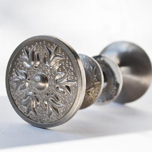 May include: Silver door knob with a decorative floral design. The knob is round and has a detailed pattern.