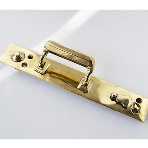 May include: A brass door handle with a rectangular plate and a lever handle. The handle has a decorative design and is polished to a shine.