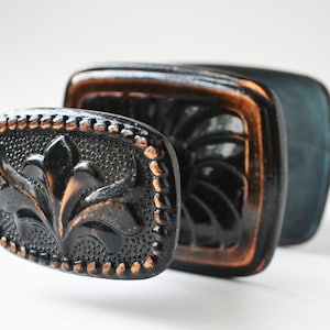 Puede incluir: Pomo de puerta decorativo negro y cobre con un diseño floral. El pomo tiene una superficie texturizada y un borde elevado.