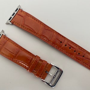 May include: Two orange leather watch bands with silver clasps and stitching. The bands are designed for Apple Watches.