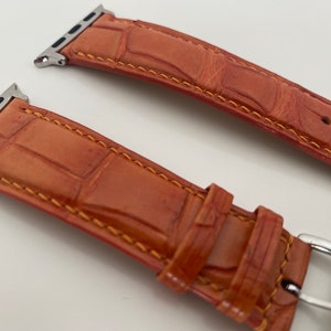 May include: Two orange leather watch bands with silver clasps. The bands have a crocodile pattern and are stitched with orange thread.