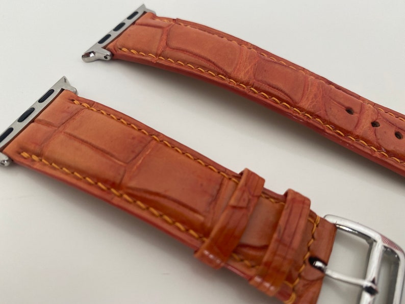 May include: Two orange leather watch bands with silver clasps. The bands have a crocodile pattern and are stitched with orange thread.