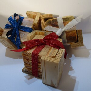 May include: Set of four wooden coasters with a natural wood finish. The coasters are stacked and tied together with red and blue ribbon. The coasters are decorated with a bow and glitter.