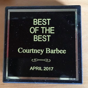 May include: Black plaque with a gold border and the text "BEST OF THE BEST" in yellow lettering. The name "Courtney Barbee" is also in yellow lettering. The date "APRIL 2017" is in yellow lettering at the bottom.