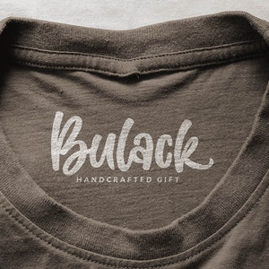 May include: A brown t-shirt with a white, handwritten logo that says "Bullock Handcrafted Gift".