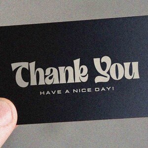 May include: A black card with white text that says "Thank You" in a stylized font. Below the text, it says "Have a nice day!"