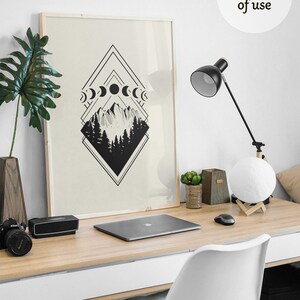 May include: A framed art print featuring a black and white geometric design with mountain and forest imagery, and moon phases. The artwork is displayed on a wooden desk with a laptop, lamp, and decorative items.
