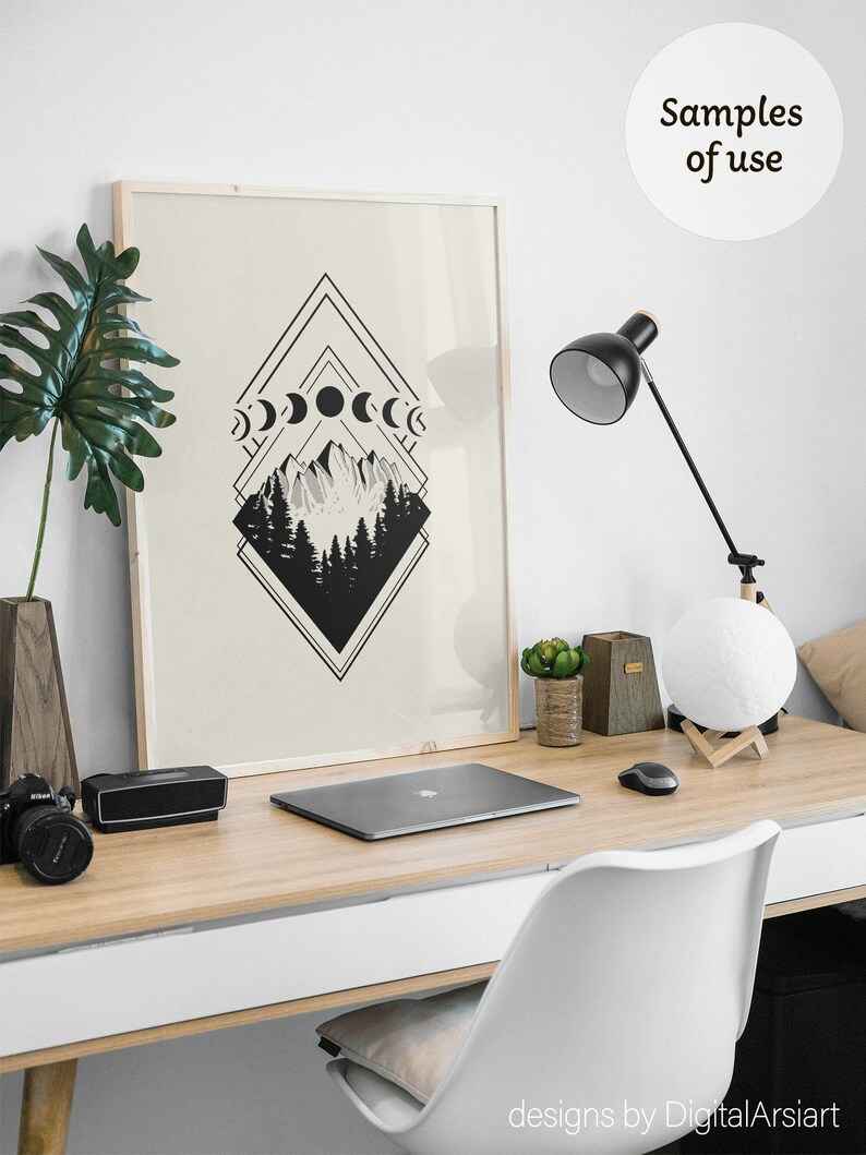 May include: A framed art print featuring a black and white geometric design with mountain and forest imagery, and moon phases. The artwork is displayed on a wooden desk with a laptop, lamp, and decorative items.
