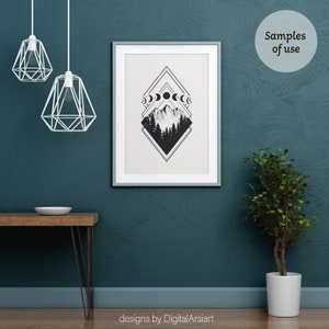 May include: A framed black and white art print featuring a mountain and forest scene with moon phases. The artwork is displayed on a teal wall. The image also shows a wooden table, a potted plant, and two geometric pendant lights.