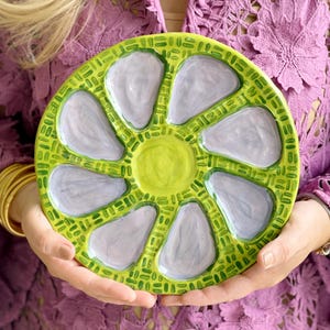 May include: A round ceramic plate with six individual serving sections. The plate is decorated with a green and white pattern and has a light purple glaze.