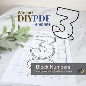 May include: A black wire sculpture shaped like the number three, accompanied by a printed paper template featuring a grid and the number three outline. The text on the paper reads Wire art DIY PDF Template and Block Numbers Templates with & without base.