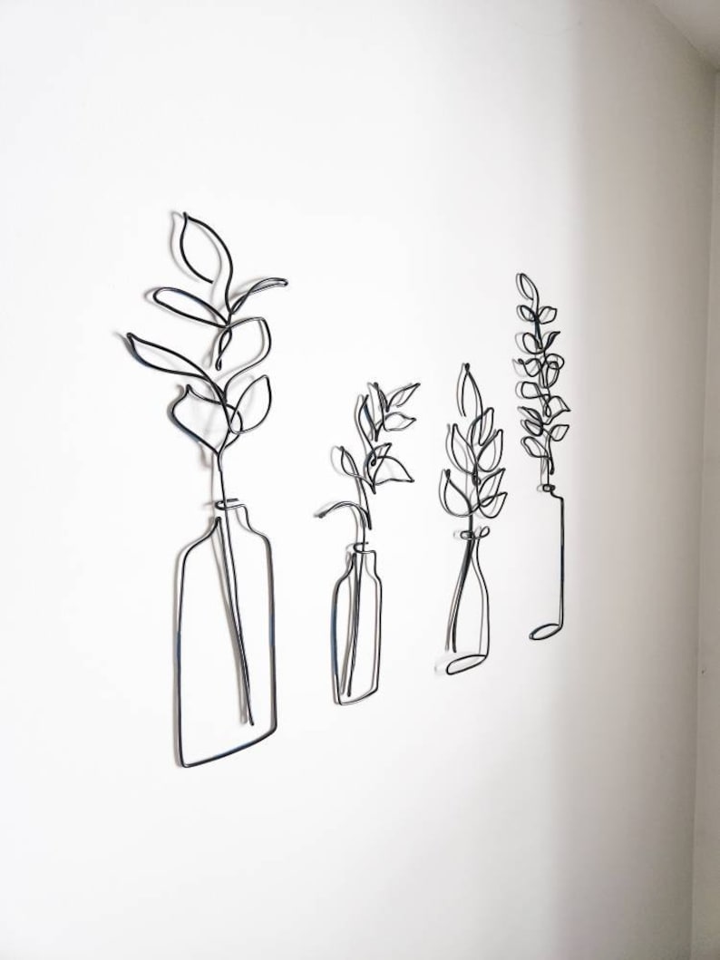 May include: Four black wire art pieces depicting stylized plants in vases, mounted on a white wall. The pieces vary in size and shape, with the leaves and vases outlined in a continuous wire form. The minimalist design adds a modern touch to the decor.