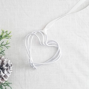 May include: A silver wire heart ornament with a white ribbon for hanging. The heart is made of multiple layers of wire, creating a three-dimensional effect.