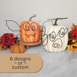 May include: Two pumpkins decorated with wire. One pumpkin is orange and has a bat design with eyes and fangs. The other pumpkin is white and has the word "Boo" written in wire. The text below the pumpkins says "6 designs ~ or ~ custom".