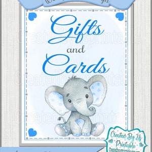 May include: A baby shower sign with a blue ribbon banner that reads "Baby Shower Sign". The sign has a blue and gray border with the words "Gifts and Cards" in blue script. A watercolor illustration of a gray elephant with blue polka dots is in the center.