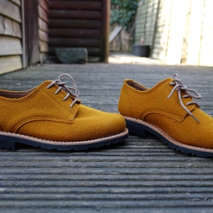May include: A pair of mustard yellow felt lace-up shoes with brown laces and a black rubber sole.