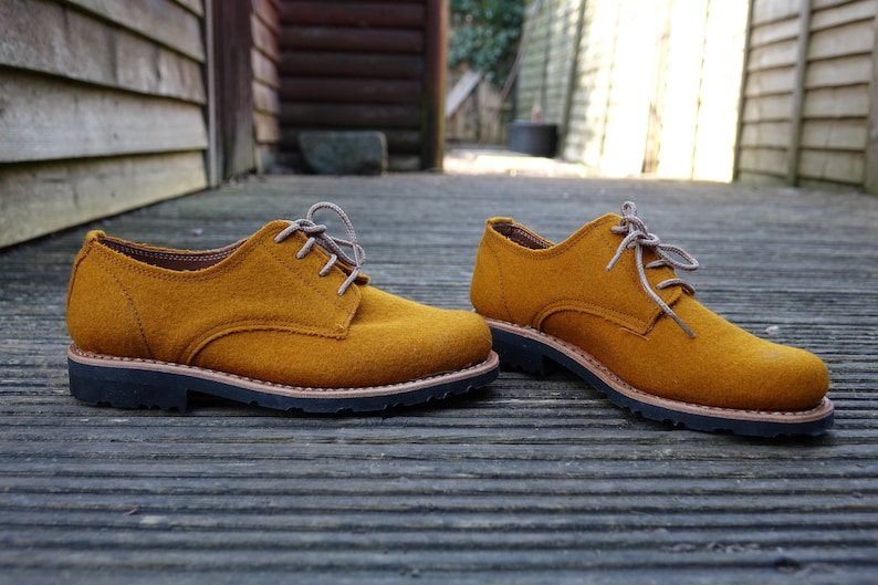 May include: A pair of mustard yellow felt lace-up shoes with brown laces and a black rubber sole.