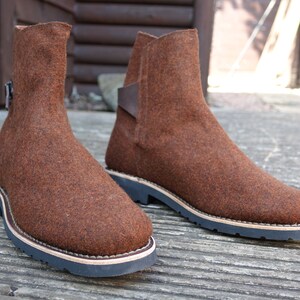 May include: A pair of brown felt ankle boots with a leather strap and buckle detail. The boots have a thick rubber sole.