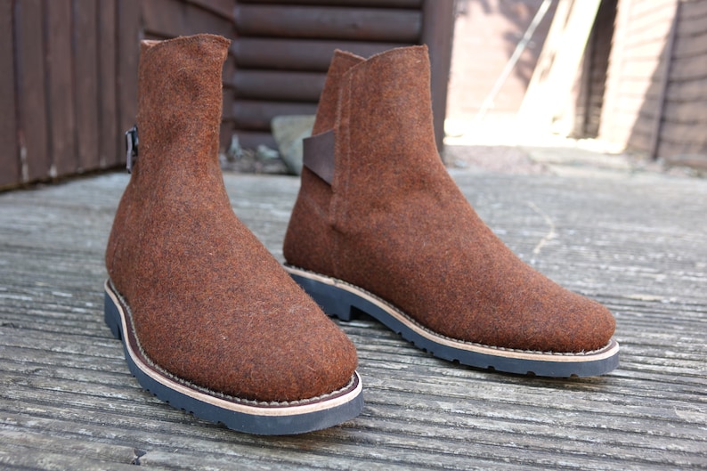 May include: A pair of brown felt ankle boots with a leather strap and buckle detail. The boots have a thick rubber sole.