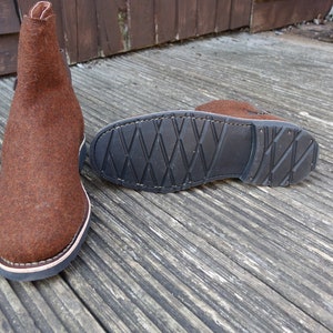 May include: A pair of brown felt boots with a black rubber sole. The boots have a simple design and are made of a soft, comfortable material.