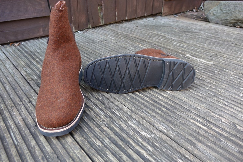 May include: A pair of brown felt boots with a black rubber sole. The boots have a simple design and are made of a soft, comfortable material.