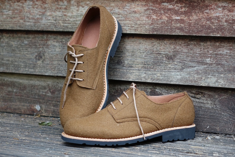 May include: A pair of brown leather lace-up shoes with a dark brown sole. The shoes are on a wooden surface.