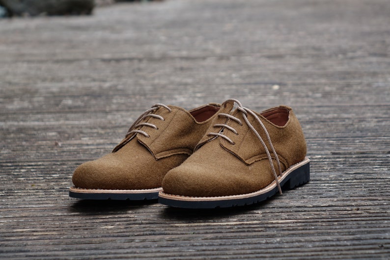 May include: A pair of brown suede lace-up shoes with a black rubber sole.