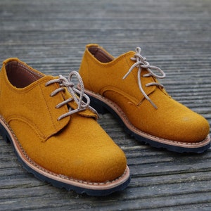 May include: A pair of mustard yellow lace-up shoes with brown soles. The shoes are made of a soft, suede-like material.