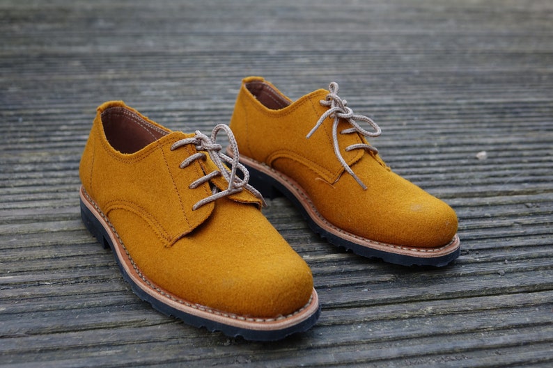May include: A pair of mustard yellow lace-up shoes with brown soles. The shoes are made of a soft, suede-like material.