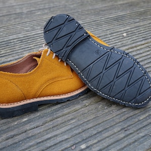 May include: A pair of mustard yellow suede shoes with black rubber soles. The shoes have a lace-up closure and a classic oxford style.