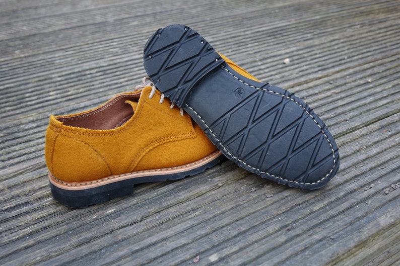 May include: A pair of mustard yellow suede shoes with black rubber soles. The shoes have a lace-up closure and a classic oxford style.