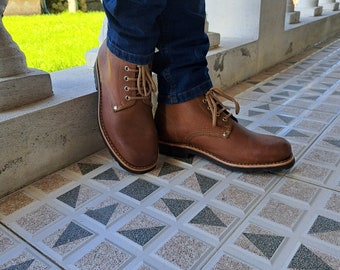May include: Brown leather boots with a lace-up design. The boots have a classic style with a rounded toe and a sturdy sole. The laces and stitching are in a matching brown color. The boots are worn with blue jeans.