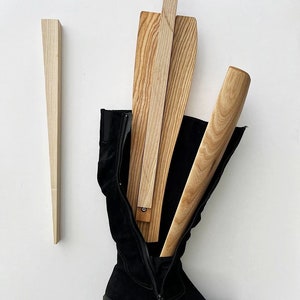 May include: A pair of black suede knee-high boots with a zipper on the side. The boots are being stretched with wooden boot stretchers.