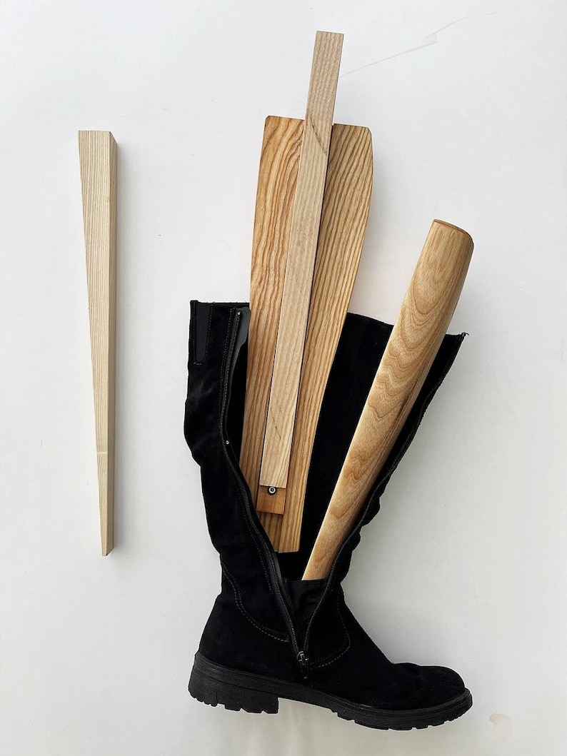 May include: A pair of black suede knee-high boots with a zipper on the side. The boots are being stretched with wooden boot stretchers.