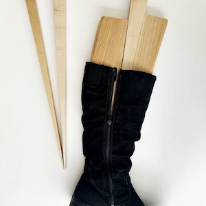 May include: A pair of black suede knee-high boots with a zipper up the back. The boots are being held up by three wooden boot shapers.