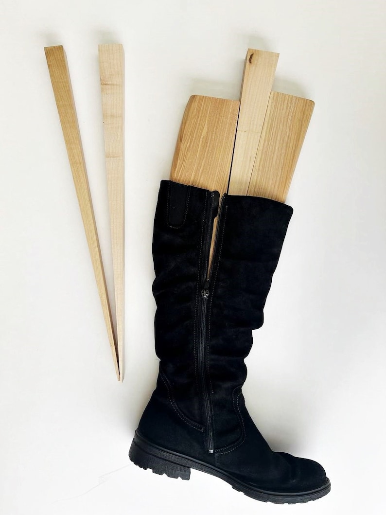 May include: A pair of black suede knee-high boots with a zipper up the back. The boots are being held up by three wooden boot shapers.