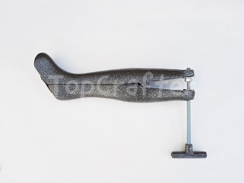 May include: A gray shoe stretcher with a metal screw and a T-shaped handle. The stretcher is designed to help stretch shoes to a wider fit.