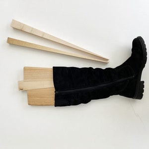 May include: A pair of wooden boot stretchers with a black knee-high boot on top. The boot stretchers are made of light wood and are designed to help keep boots in shape.
