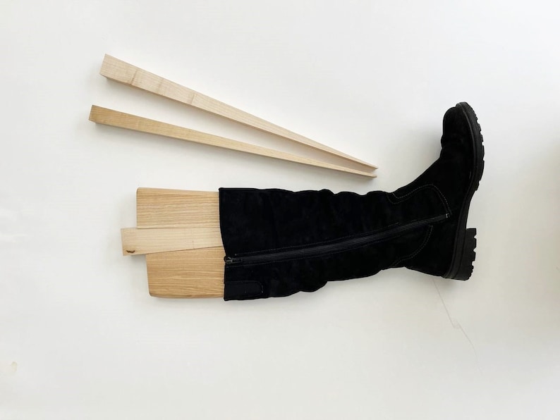May include: A pair of wooden boot stretchers with a black knee-high boot on top. The boot stretchers are made of light wood and are designed to help keep boots in shape.
