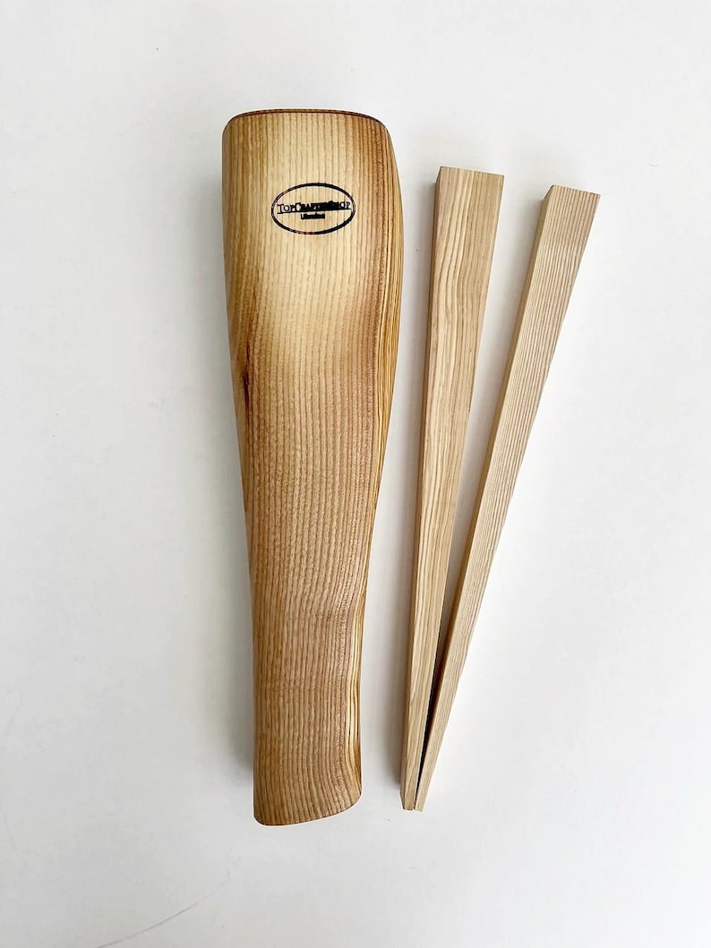 May include: Wooden kitchen tongs with a natural wood finish. The tongs are made of two long, thin pieces of wood that are joined together at the top. The tongs are designed to be used for picking up and holding food.