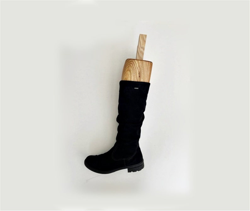 May include: Black suede boot with a wooden shoe tree inside. The boot is on a white background.